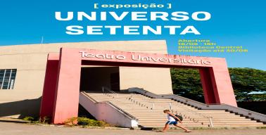 A imagem é uma fotografia em cores tirada em um dia ensolarado, com céu azul intenso ao fundo. Em destaque, está a fachada do Teatro Universitário, um edifício de concreto claro com uma grande estrutura em forma de pórtico retangular na cor vermelha, que emoldura a escadaria de acesso. Acima da escadaria, em letras curvas brancas, lê-se “Teatro Universitário”. No canto inferior direito da imagem, um jovem de pele parda, vestindo regata branca, short azul e mochila preta, caminha na calçada em frente à escad